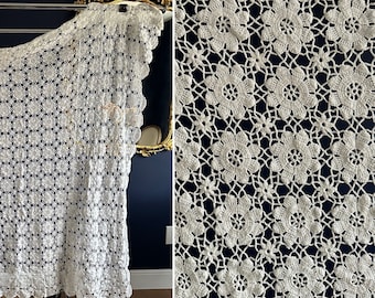 Könnte beinhalten: Weiße Häkeltischdecke mit Blumenmuster. Die Tischdecke ist aus zarter Spitze und hat einen gewellten Rand.