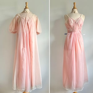 Puede incluir: Dos camisones rosas vintage exhibidos en maniquíes. El primero es un camisón largo y transparente con mangas cortas y un escote con ribete de encaje. El segundo es un camisón tipo slip con tirantes finos y un corpiño fruncido. Ambos camisones tienen un diseño largo y fluido.