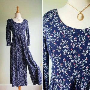 May include: A long-sleeved, navy blue dress with a floral print. The dress has a round neckline and a fitted bodice. The skirt is full and flows to the ankles.