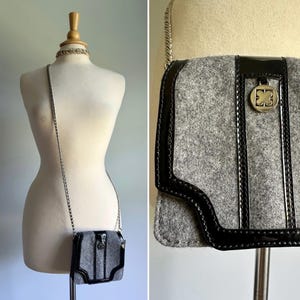 May include: A gray felt crossbody bag with a black patent leather trim and a silver chain strap. The bag has a silver metal clasp with a logo on the front.