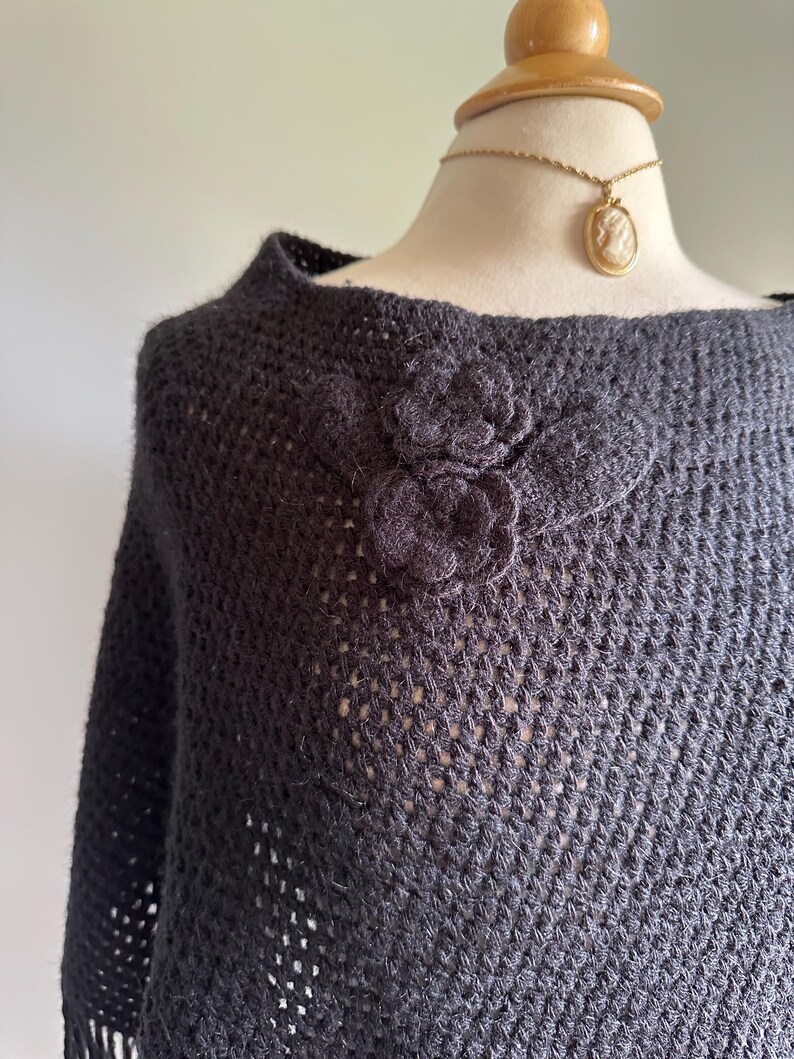 May include: Black crochet poncho with a large black flower embellishment. The poncho has a loose fit and a wide neckline.
