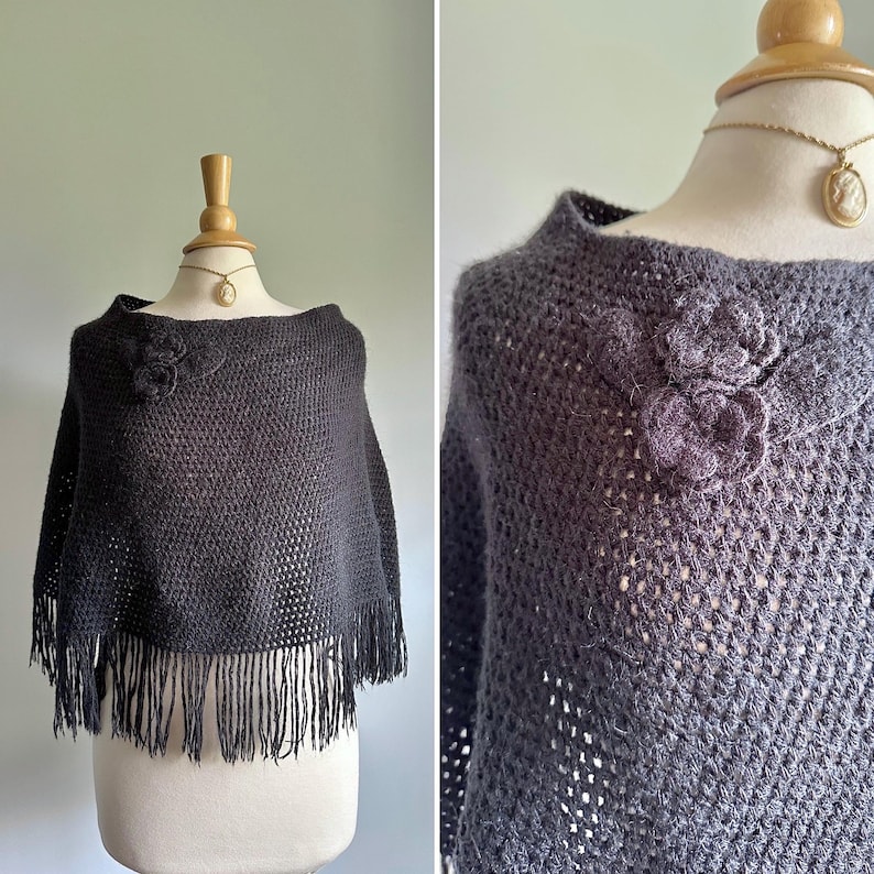May include: A dark gray crochet poncho with a fringe border and a floral design on the front.