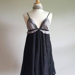 K&ouml;nnte beinhalten: Ein schwarzes Spitzenkleid mit einem grauen und schwarzen Samt-Oberteil. Das Kleid hat einen R&uuml;schen-Ausschnitt und ein tailliertes Oberteil. Der Rock ist weit und flie&szlig;end.