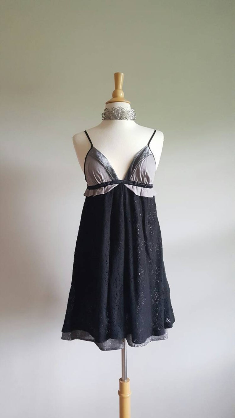 K&ouml;nnte beinhalten: Ein schwarzes Spitzenkleid mit einem grauen und schwarzen Samt-Oberteil. Das Kleid hat einen R&uuml;schen-Ausschnitt und ein tailliertes Oberteil. Der Rock ist weit und flie&szlig;end.