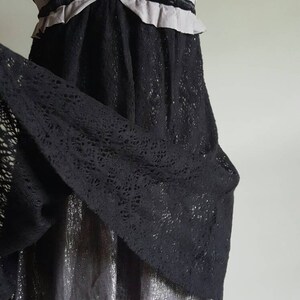 K&ouml;nnte beinhalten: Ein schwarzes Spitzenkleid mit einem mehrlagigen Oberteil in Silber und Grau. Das Oberteil hat einen Samtbesatz und einen R&uuml;schenkragen.