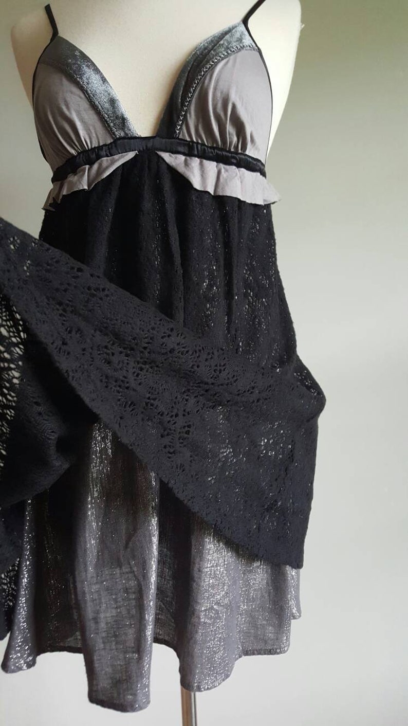 K&ouml;nnte beinhalten: Ein schwarzes Spitzenkleid mit einem mehrlagigen Oberteil in Silber und Grau. Das Oberteil hat einen Samtbesatz und einen R&uuml;schenkragen.