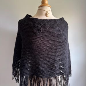 May include: Black knitted poncho with a floral design and fringe trim.