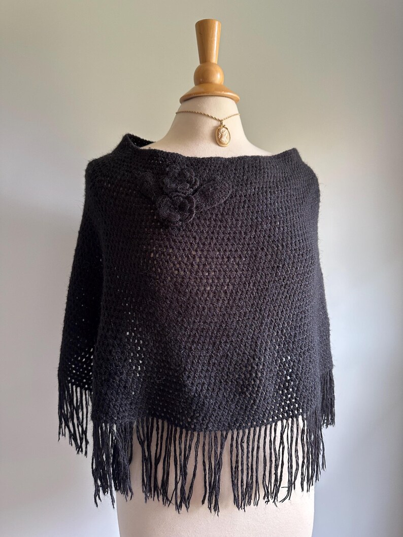 May include: Black knitted poncho with a floral design and fringe trim.