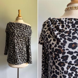 Puede incluir: Top de manga larga con estampado de leopardo. La parte superior se muestra en un maniquí y presenta un cuello de cisne y un ajuste relajado. El estampado incluye manchas negras y marrones sobre un fondo beige claro.