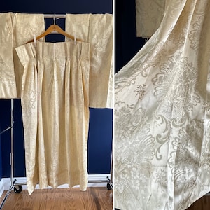 Puede incluir: Un par de cortinas de damasco de color crema con un patrón floral. Las cortinas están colgadas de una barra de metal y están plisadas en la parte superior.