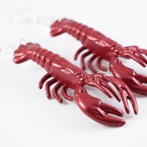 May include: A pair of red lobster earrings. The lobsters are made of a shiny, metallic material and have a detailed design.