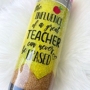 Puede incluir: Un vaso amarillo con purpurina con un dise&ntilde;o de l&aacute;piz en blanco y negro. El vaso tiene el texto "The influence of a great teacher can never be erased".