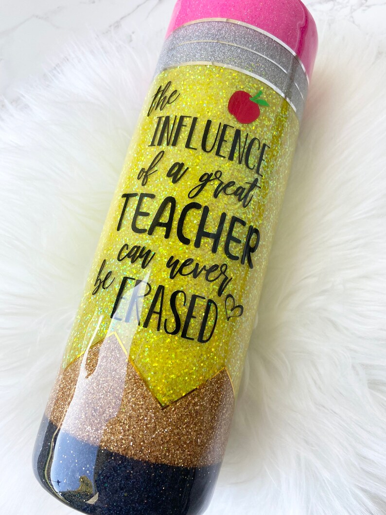 Puede incluir: Un vaso amarillo con purpurina con un dise&ntilde;o de l&aacute;piz en blanco y negro. El vaso tiene el texto "The influence of a great teacher can never be erased".