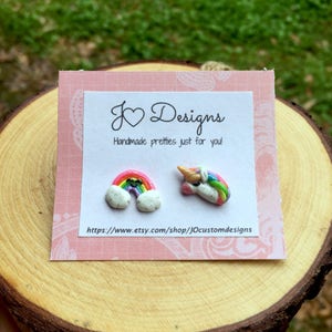 May include: A pair of handmade polymer clay earrings featuring a rainbow and a unicorn. The earrings are on a pink card with the text "J&hearts;Designs Handmade pretties just for you! https://www.etsy.com/shop/jOcustomdesigns"