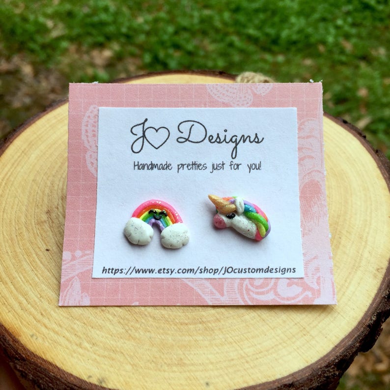 May include: A pair of handmade polymer clay earrings featuring a rainbow and a unicorn. The earrings are on a pink card with the text "J&hearts;Designs Handmade pretties just for you! https://www.etsy.com/shop/jOcustomdesigns"