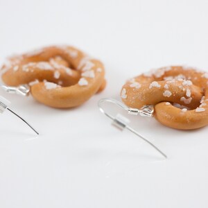 Puede incluir: Un par de pendientes con forma de pretzel con cristales de sal, hechos de arcilla polim&eacute;rica. Los pendientes son plateados y tienen un cierre de gancho.