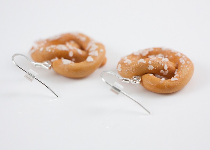 Puede incluir: Un par de pendientes con forma de pretzel con cristales de sal, hechos de arcilla polim&eacute;rica. Los pendientes son plateados y tienen un cierre de gancho.