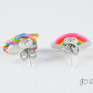 May include: A pair of stud earrings featuring a rainbow unicorn and a rainbow on a white cloud. The earrings are silver and have a post back.