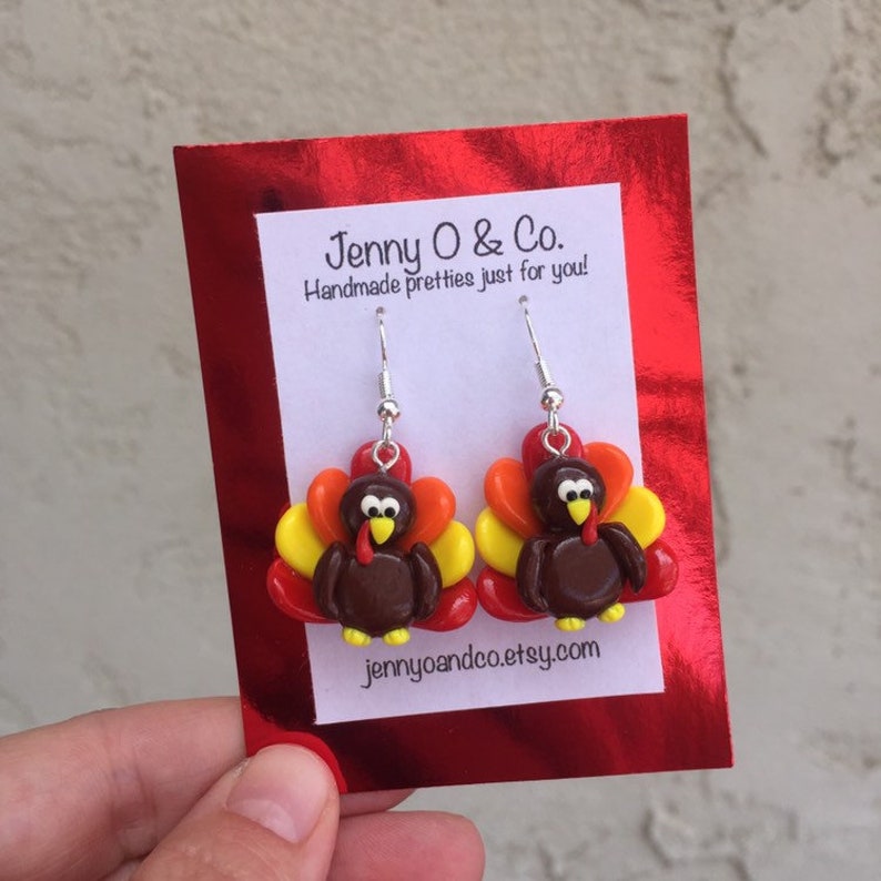 May include: A pair of dangle earrings featuring a brown turkey with red, orange, and yellow feathers. The earrings are on a white card with the text "Jenny O & Co. Handmade pretties just for you!" and the website "jennyoandco.etsy.com".