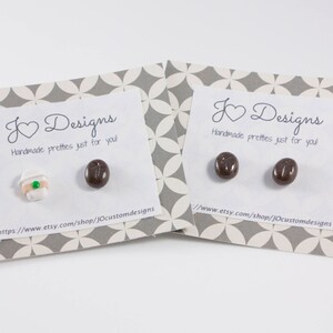 May include: A pair of earrings featuring a coffee cup and a coffee bean design. The earrings are handmade and come on a card with the text "K Designs Handmade pretties just for you!" and a website address.