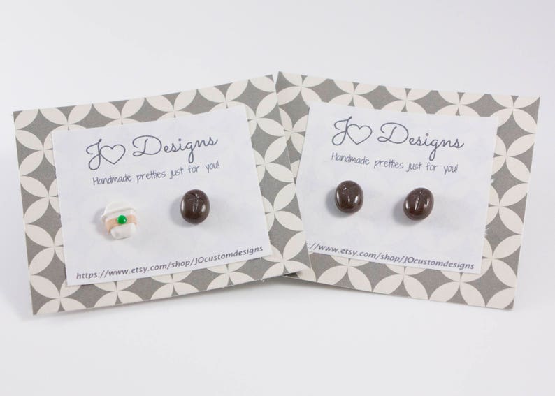 May include: A pair of earrings featuring a coffee cup and a coffee bean design. The earrings are handmade and come on a card with the text "K Designs Handmade pretties just for you!" and a website address.