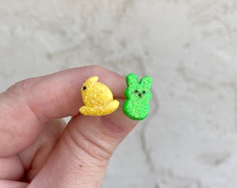 Könnte beinhalten: Ein Paar pastellfarbene Ohrringe in Hasenform. Ein Ohrring ist gelb und der andere grün.