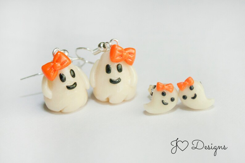 May include: A set of three ghost earrings with orange bows. The earrings are made of white polymer clay and have black eyes and a smiling mouth. The earrings are perfect for Halloween or any spooky occasion.