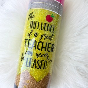 Puede incluir: Un vaso amarillo con purpurina con una parte superior negra y plateada con purpurina. El vaso tiene un dise&ntilde;o de l&aacute;piz con el texto "the INFLUENCE of a great TEACHER can never be ERASED".