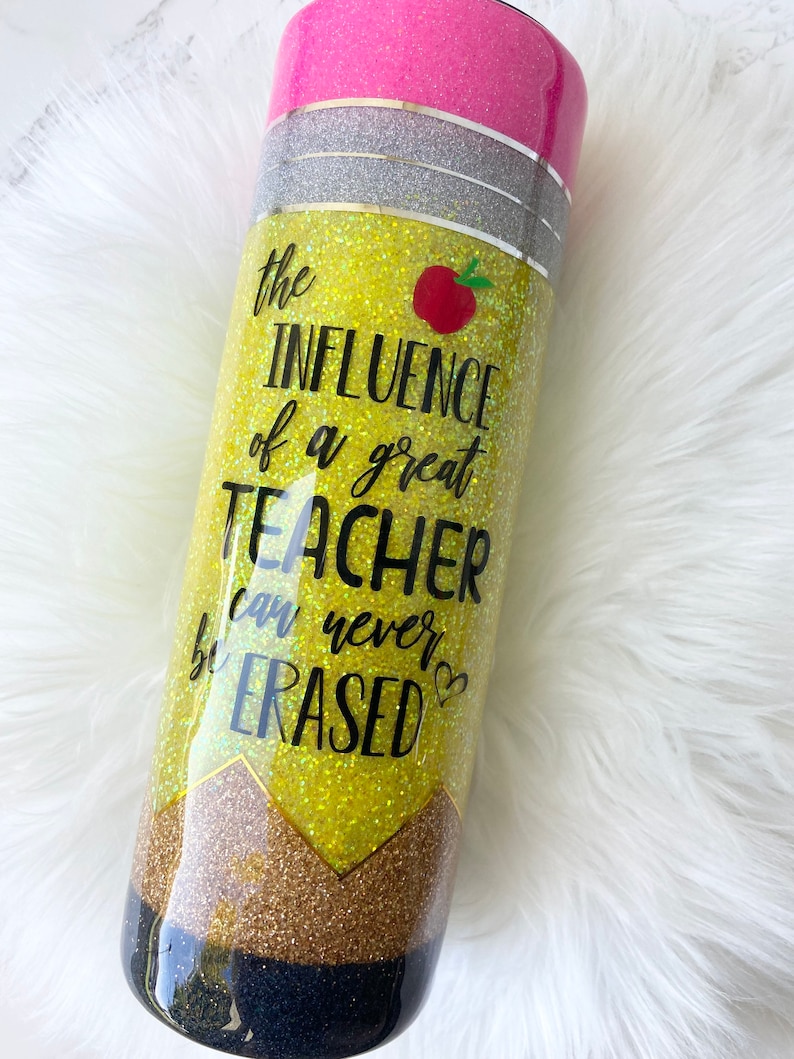 Puede incluir: Un vaso amarillo con purpurina con una parte superior negra y plateada con purpurina. El vaso tiene un dise&ntilde;o de l&aacute;piz con el texto "the INFLUENCE of a great TEACHER can never be ERASED".