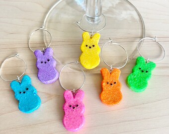 Könnte beinhalten: Sechs bunte Weinglas-Anhänger in Form von Osterhasen. Die Anhänger sind aus Glitzer und in den Farben Blau, Lila, Gelb, Orange, Grün und Pink erhältlich.