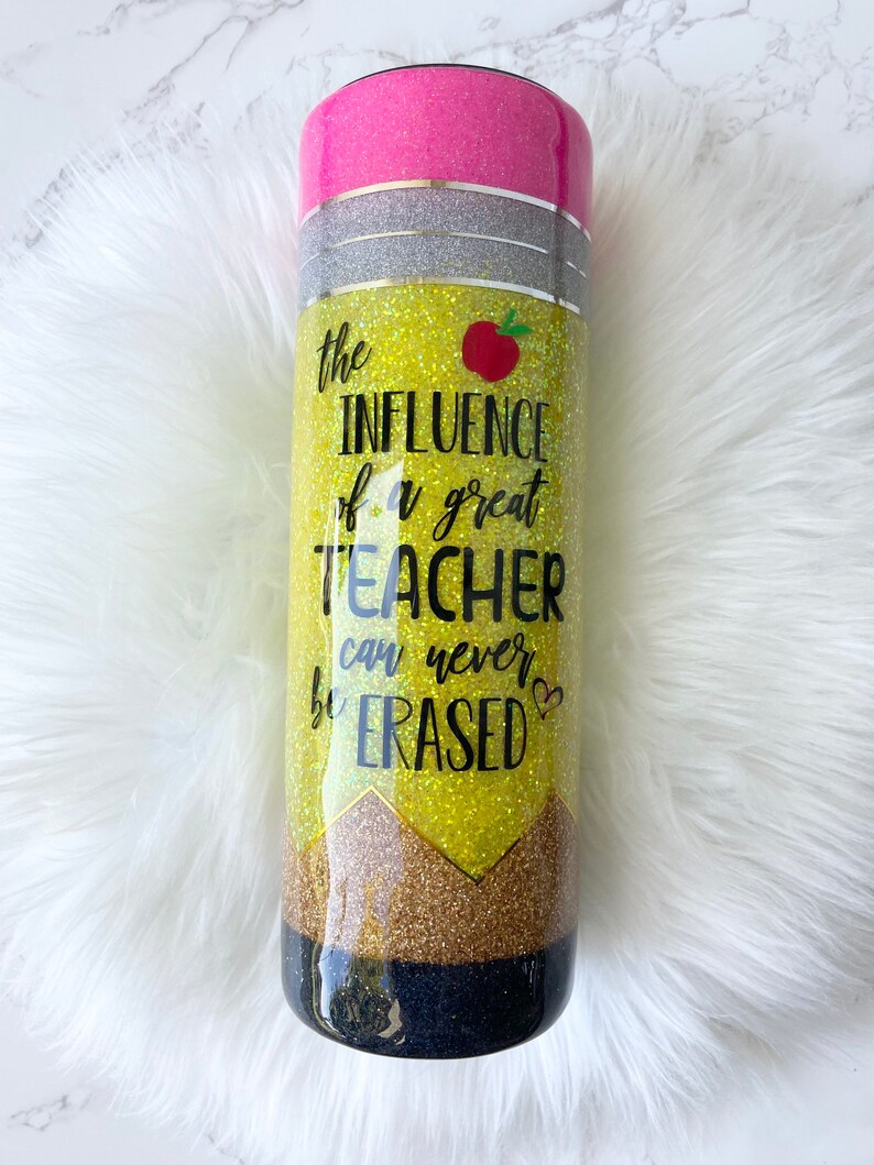 Puede incluir: Un vaso de glitter amarillo y negro con una tapa rosa. El vaso tiene un dise&ntilde;o de l&aacute;piz y el texto "the INFLUENCE of a great TEACHER can never be ERASED".