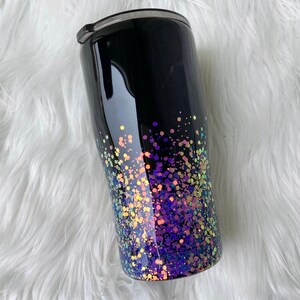 May include: A black stainless steel tumbler with a glittery ombre design. The glitter is iridescent and fades from purple to yellow.