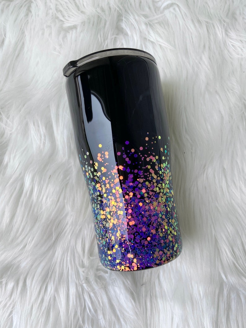 May include: A black stainless steel tumbler with a glittery ombre design. The glitter is iridescent and fades from purple to yellow.