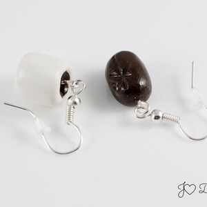 May include: A pair of earrings with a white and brown ceramic design. The white earring is shaped like a mug and the brown earring is shaped like a coffee bean.