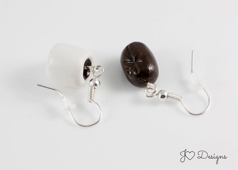 May include: A pair of earrings with a white and brown ceramic design. The white earring is shaped like a mug and the brown earring is shaped like a coffee bean.