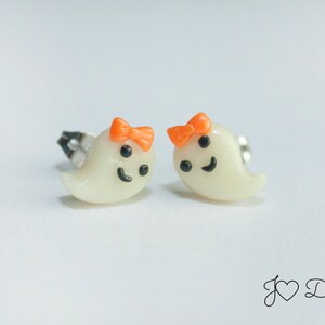 May include: A pair of white ghost-shaped earrings with orange bows and black facial features.