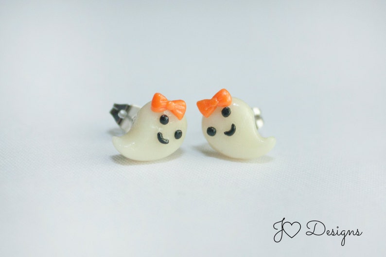 May include: A pair of white ghost-shaped earrings with orange bows and black facial features.