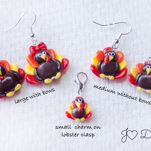 May include: Three pairs of polymer clay turkey earrings in different sizes. The largest pair has red bows. The medium pair does not have bows. The smallest turkey is a charm on a lobster clasp.  "J &hearts; Designs" is written in the bottom right corner.