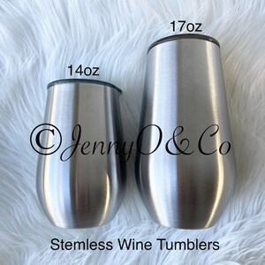 May include: Two stainless steel stemless wine tumblers, one 14 oz and one 17 oz. The tumblers are silver and have a brushed finish. The tumblers are on a white fluffy surface. The text "Jenny O & Co" is visible on the tumblers.