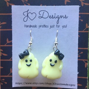 May include: A pair of yellow ghost earrings with black bows and a happy face. The earrings are on a white card with the text "J &hearts; Designs Handmade pretties just for you!" and a website address.