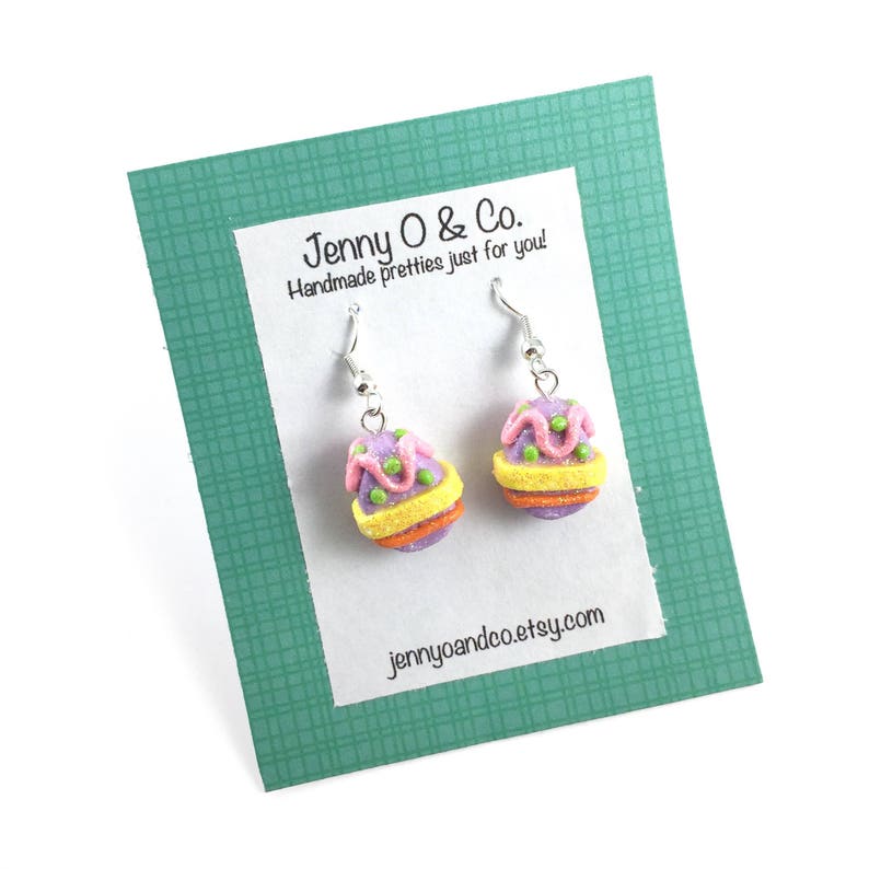 K&ouml;nnte beinhalten: Ein Paar Ohrh&auml;nger mit einem Design aus lila, rosa, gelben und gr&uuml;nen Ostereiern. Die Ohrringe befinden sich auf einer wei&szlig;en Karte mit dem Text "Jenny O & Co. Handmade pretties just for you! jennyoandco.etsy.com"