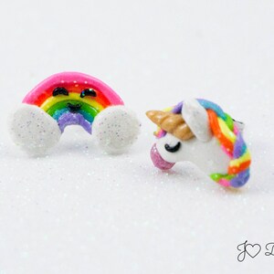 May include: A pair of colorful rainbow and unicorn earrings. The rainbow earring is pink with a smiling face and white clouds. The unicorn earring is white with a rainbow mane and horn.