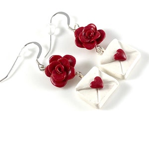 May include: A pair of dangle earrings featuring a red rose charm and a white envelope charm with a red heart on the front.