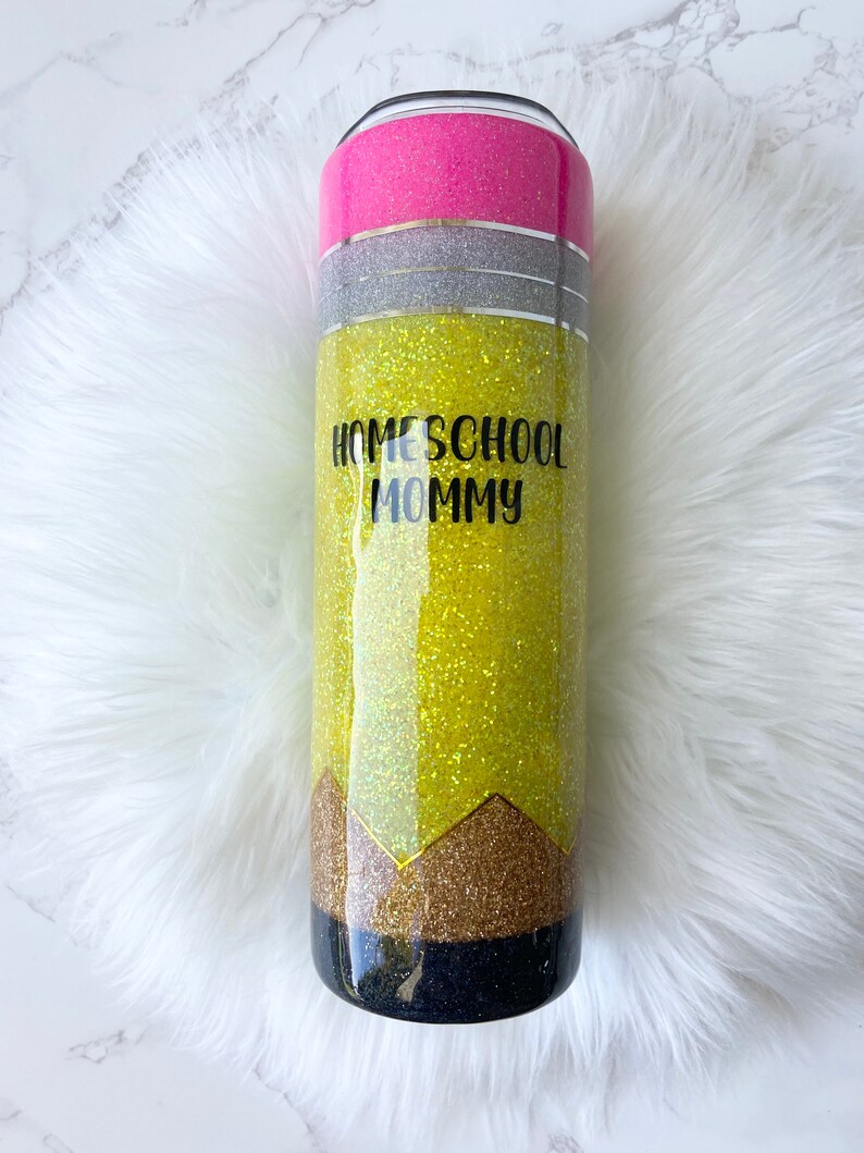 Puede incluir: Un vaso amarillo cubierto de purpurina con un dise&ntilde;o de l&aacute;piz negro y dorado. El vaso tiene el texto "HOMESCHOOL MOMMY" en la parte delantera.