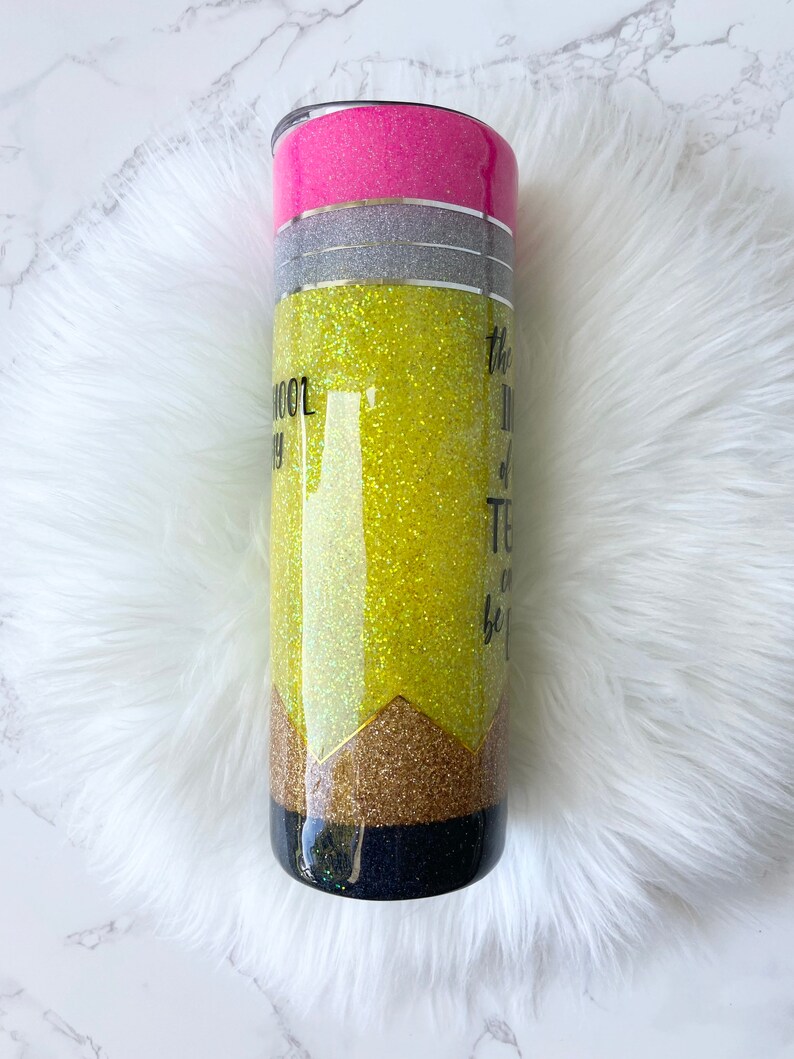 Puede incluir: Un vaso amarillo con purpurina con un dise&ntilde;o de l&aacute;piz negro y dorado. El vaso tiene una tapa rosa y una banda plateada alrededor del medio. El texto en el vaso dice "La mejor parte de la ense&ntilde;anza es ser..."