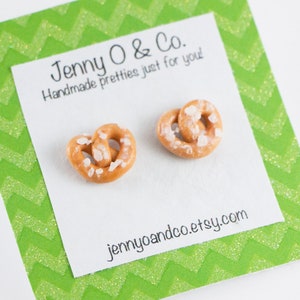 May include: A pair of earrings shaped like pretzels with white sprinkles. The earrings are on a white card with green chevron patterned paper around the edges. The card says "Jenny O & Co. Handmade pretties just for you" and "jennyoandco.etsy.com".