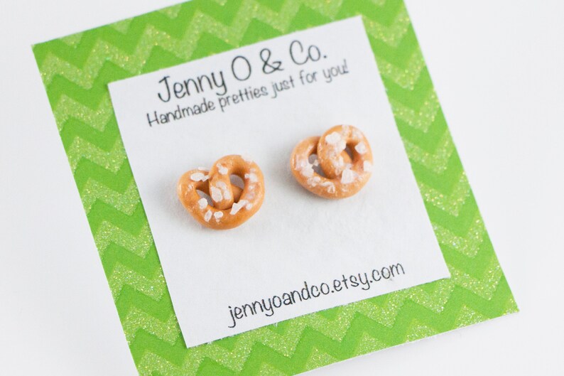 May include: A pair of earrings shaped like pretzels with white sprinkles. The earrings are on a white card with green chevron patterned paper around the edges. The card says "Jenny O & Co. Handmade pretties just for you" and "jennyoandco.etsy.com".