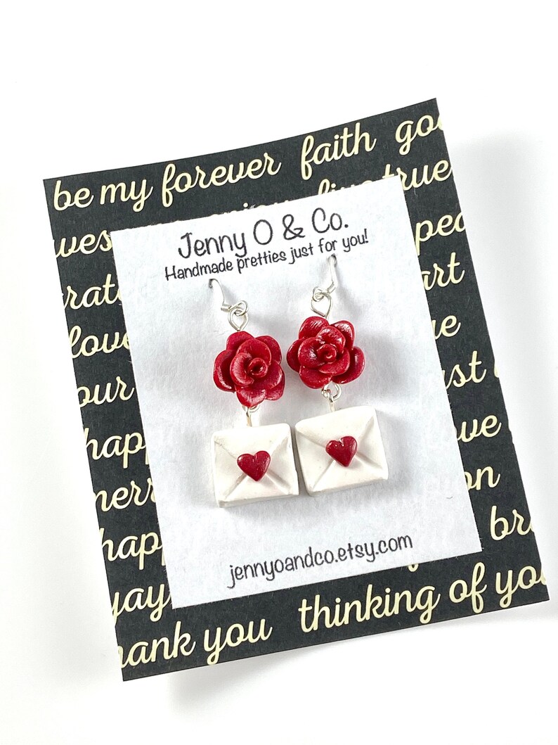 May include: Red rose and white envelope dangle earrings with a heart detail. The earrings are on a white card with the text "Jenny O & Co. Handmade pretties just for you!" and "jennyoandco.etsy.com". The card has a black border with the text "be my forever faith go" and "thank you thinking of you".