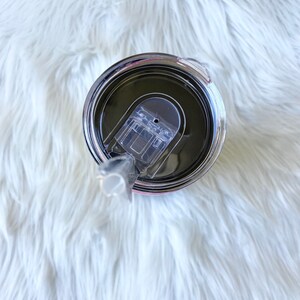 Puede incluir: Una taza de viaje de acero inoxidable con una tapa negra y una pajita de pl&aacute;stico transparente. La taza tiene un acabado plateado y una junta de goma negra alrededor de la tapa.