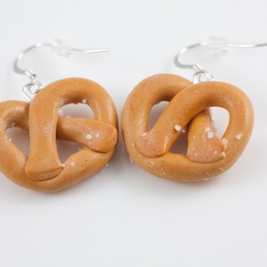 Puede incluir: Un par de pendientes de pretzel con sal y ganchos plateados. Los pretzels est&aacute;n hechos de arcilla polim&eacute;rica y tienen un aspecto realista.